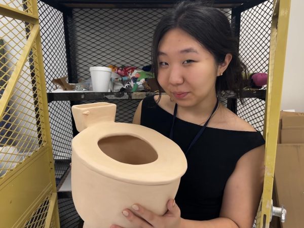 Zoe Jung, 11, holds her newest ceramic piece, a large toilet, for her AP art portfolio. Jung’s toilet is symbolic of the government, with the tank and bowl representing the government and population respectively. “[My AP art portfolio] is kind of small right now because I kind of take my time with my work.”
